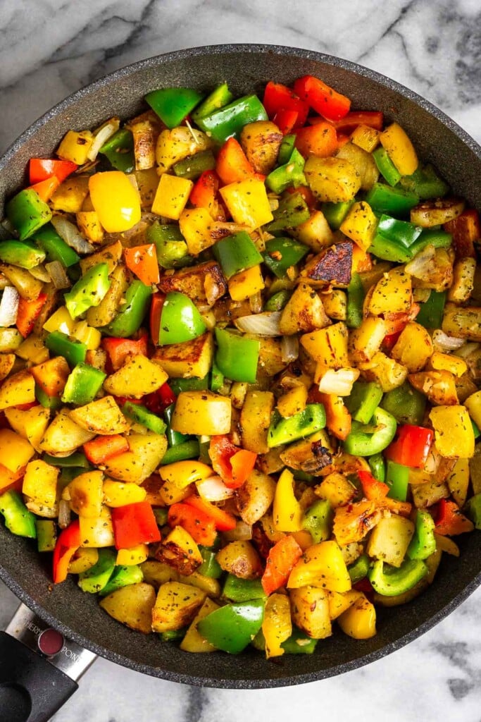 Large skillet filled with sautéed diced potatoes, bell peppers, and onions.