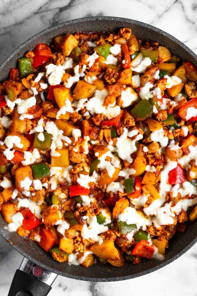 Overhead shot of mixture of ground meat, potatoes, peppers, and onions in marinara sauce topped with melted cheese in a large skillet.