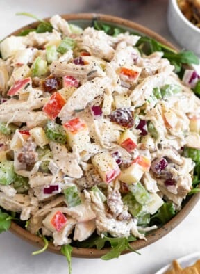 Chicken salad with apples, walnuts, celery, and dates overtop fresh arugula in a bowl.