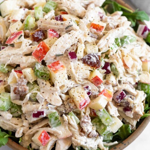 Chicken salad with apples, walnuts, celery, and dates overtop fresh arugula in a bowl.