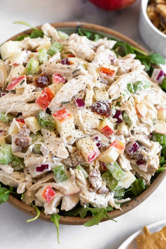Chicken salad with apples, walnuts, celery, and dates overtop fresh arugula in a bowl.