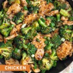Overhead shot of a large skillet filled with chicken and broccoli stir fry. It is topped with sliced green onions and sesame seeds. The pan is sitting on a tan linen.