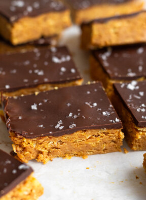 Peanut butter crunch bars topped with chocolate and flaky sea salt lined up on a piece of white parchment paper.
