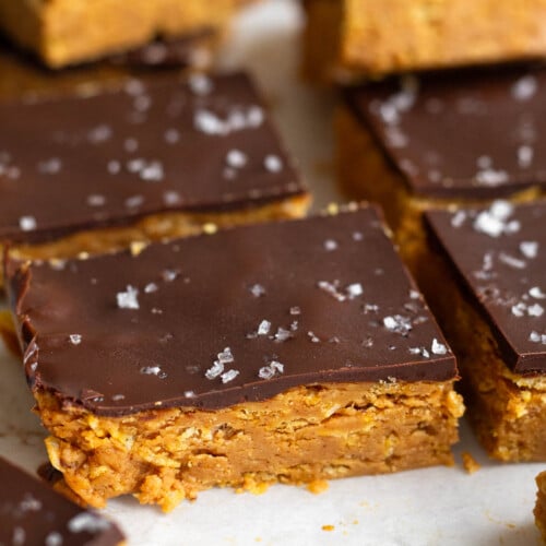 Peanut butter crunch bars topped with chocolate and flaky sea salt lined up on a piece of white parchment paper.