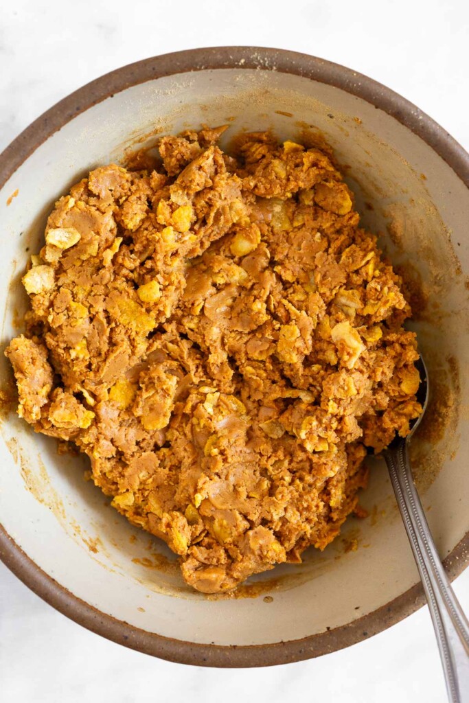 Peanut butter mixed with cornflakes in white bowl with a spoon in it.
