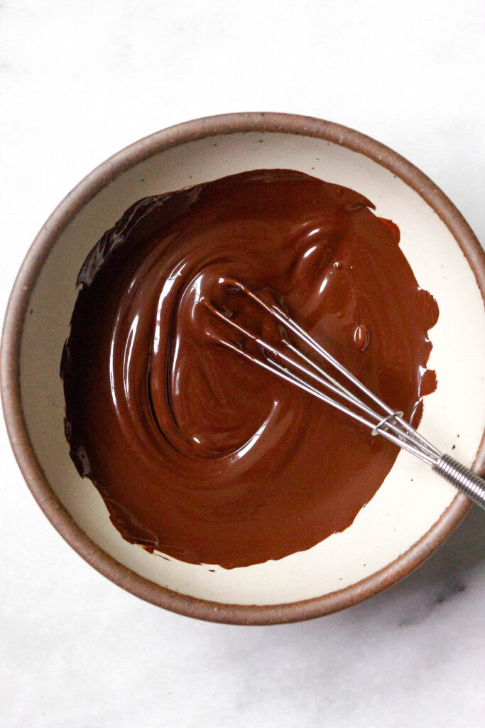 Bowl of melted dark chocolate with a small whisk in it.