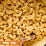 Protein mac and cheese in a large white dutch oven with a wooden spoon in it.