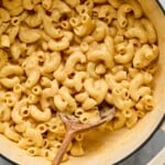 Protein mac and cheese in a large white dutch oven with a wooden spoon in it.