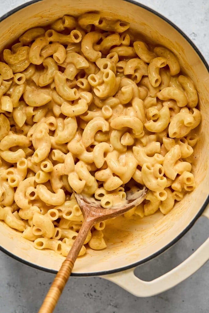 Protein mac and cheese in a large white dutch oven with a wooden spoon in it.