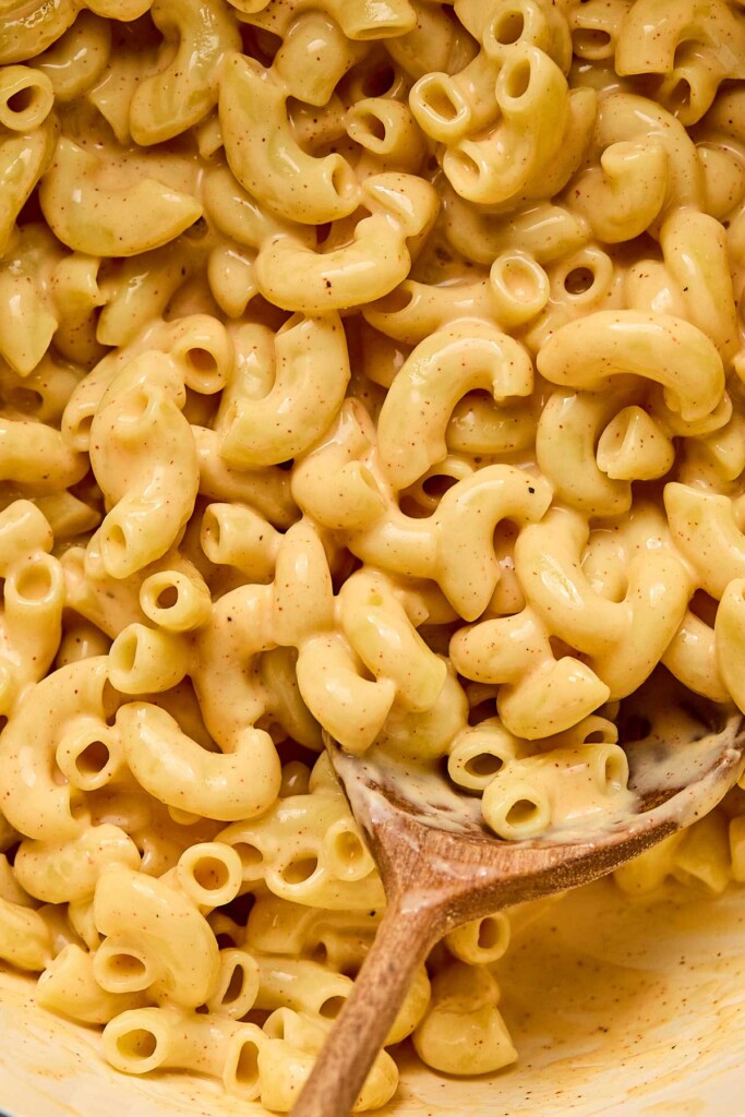 Close up of healthy mac and cheese in a large white pot with a wooden spoon in it.