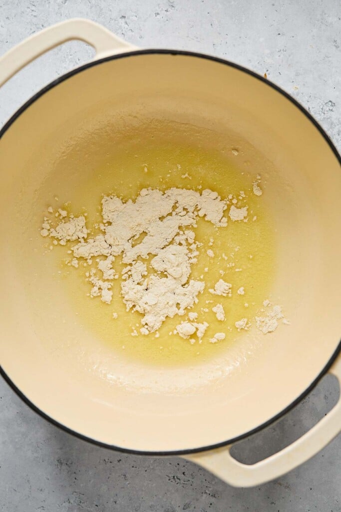 Melted butter with flour sprinkled on top of it in a large white dutch oven.