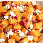 Large white bowl with roasted butternut squash with goat cheese and pomegranates tossed with a rosemary dressing.