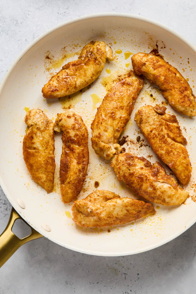 Skillet with seasoned pan fried chicken tenders in it.