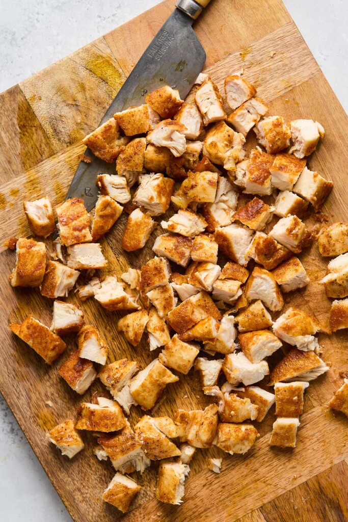 Diced seasoned chicken on a wooden cutting board with a knife next to it.