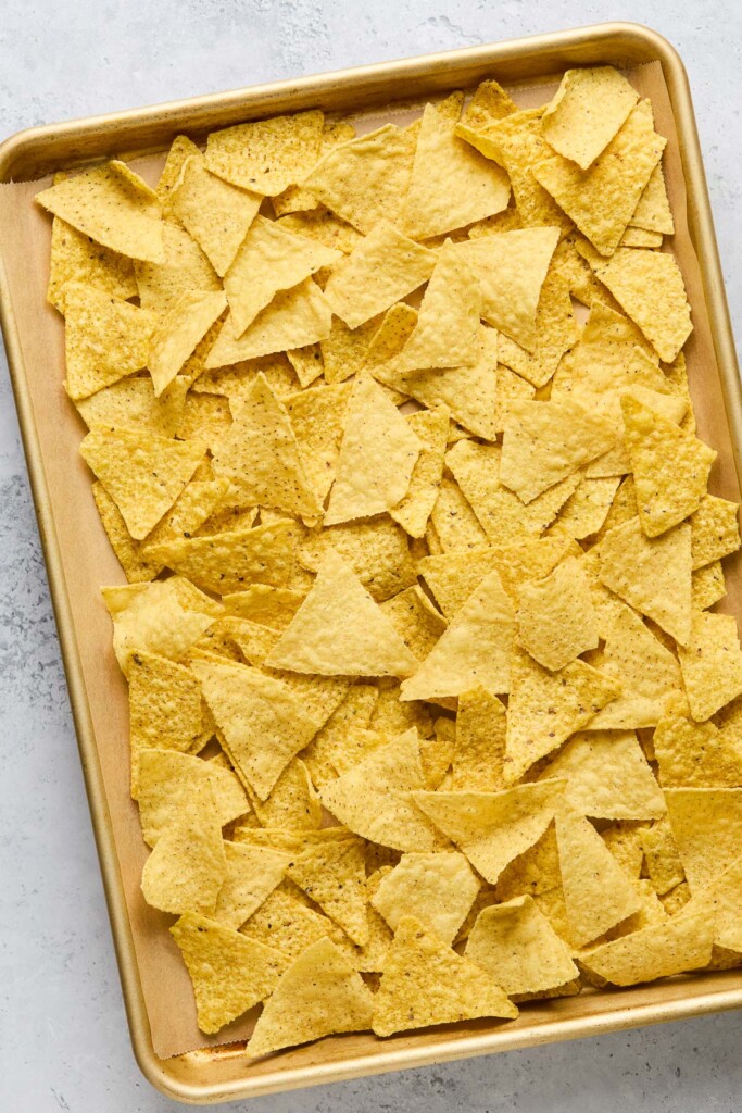 Tortilla chips spread across a baking sheet lined with parchment paper.