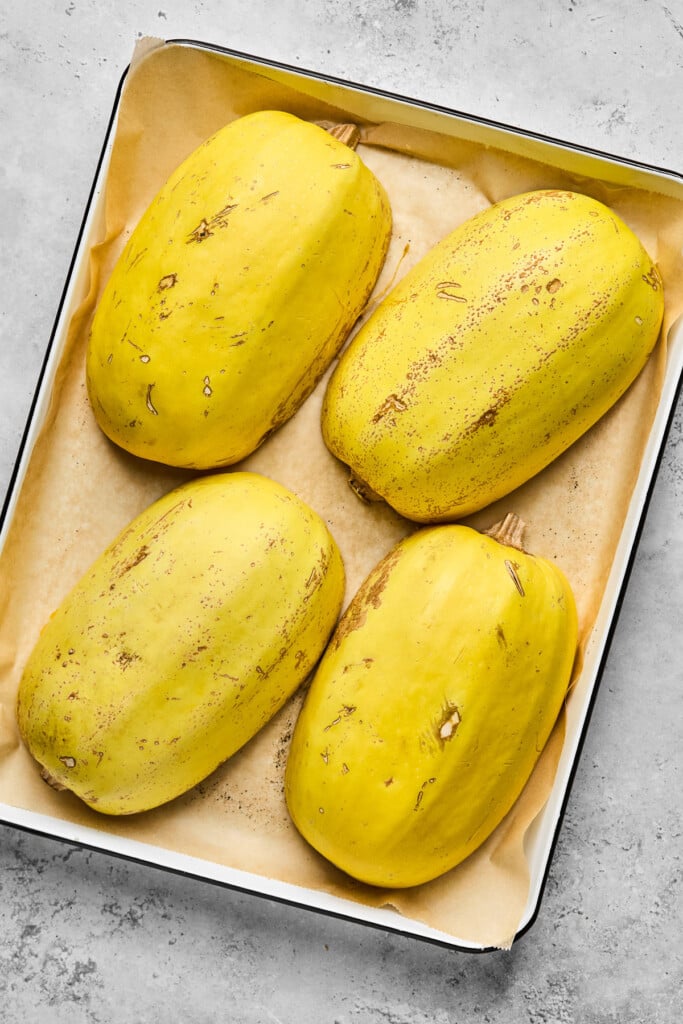 Four spaghetti squash halves cut side down on a parchment paper lined baking sheet.