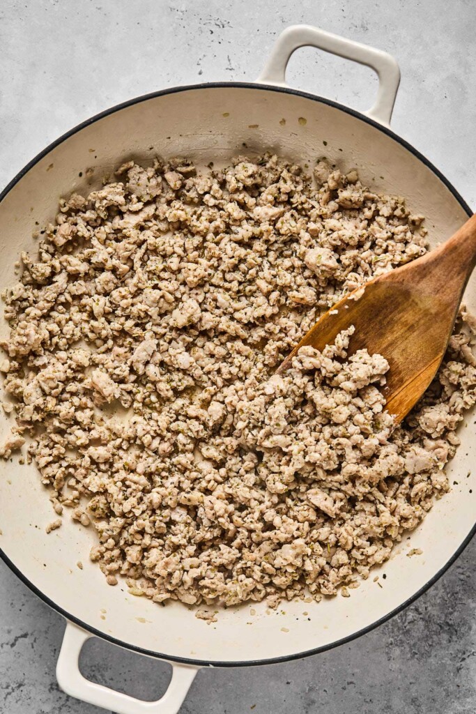 Large white skillet filled with sautéed ground chicken with a wooden spoon in it.
