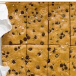 Glass pan lined with parchment paper filled with chocolate chip peanut butter perfect bar recipe.