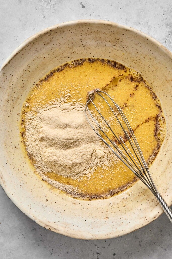 White bowl with an egg mixture in it with protein powder sprinkled overtop. There is a metal whisk in the bowl.