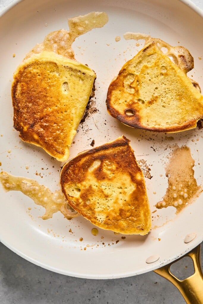 Three pieces of healthy french toast being cooked in a white skillet.