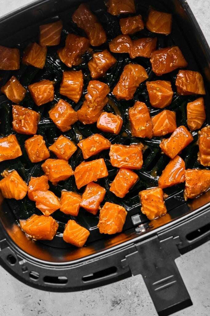Marinated raw salmon cubes in an air fryer basket.