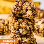 Three banana oatmeal cookies stacked on top of each other. The top one has a bite taken out of it. Around them are more cookies and in the far distance are some bananas.