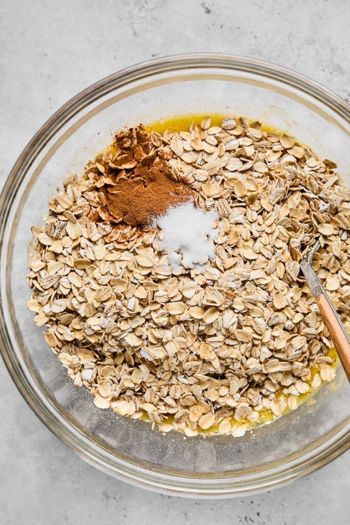 Glass bowl filled with rolled oats, cinnamon, and salt overtop a wet mixture of mashed bananas and eggs. A fork is also in the bowl.