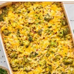 Healthy chicken broccoli rice casserole covered with melted cheese and topped with red pepper flakes and fresh parsley in a large baking dish. Next to the dish is a small bowl of parsley.