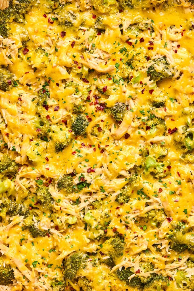 A close up of cheesy chicken broccoli rice casserole topped with red pepper flakes and fresh parsley.