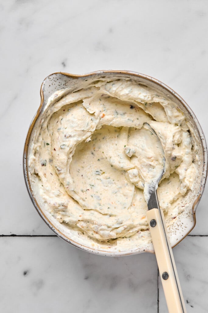 Creamy greek yogurt and cream cheese mixture with spices in a bowl with a spoon in it.