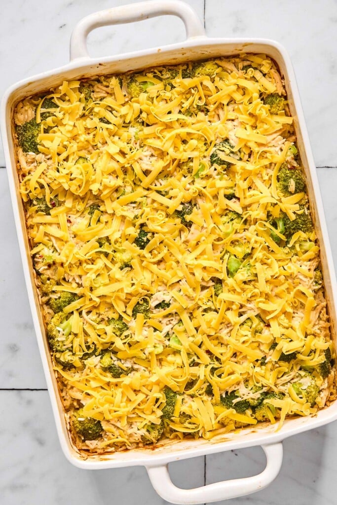 Large baking dish filled with chicken casserole that is covered with shredded cheese before it is baked.