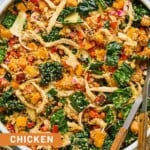 Chicken quinoa salad with butternut squash, kale, and vegges in a large white bowl. There is a fork and spoon in the bowl as well.