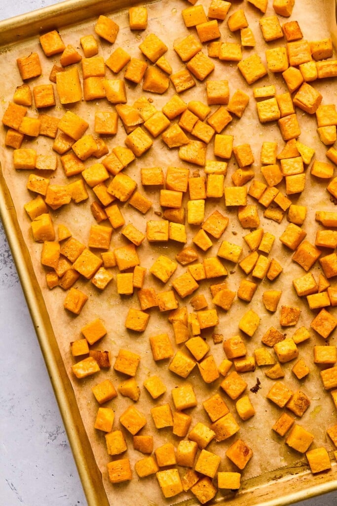 Roasted butternut squash cubes on a baking sheet lined with parchment paper.