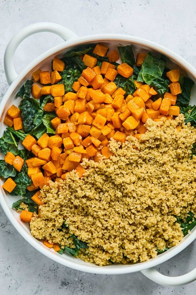 Large bowl with cubed roasted butternut squash and quinoa overtop chopped kale.