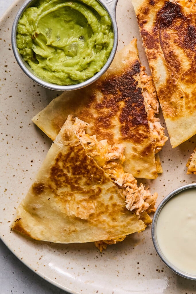 Buffalo chicken quesadillas on a plate with a cup of guacamole and a cup of blue cheese dressing for dipping.