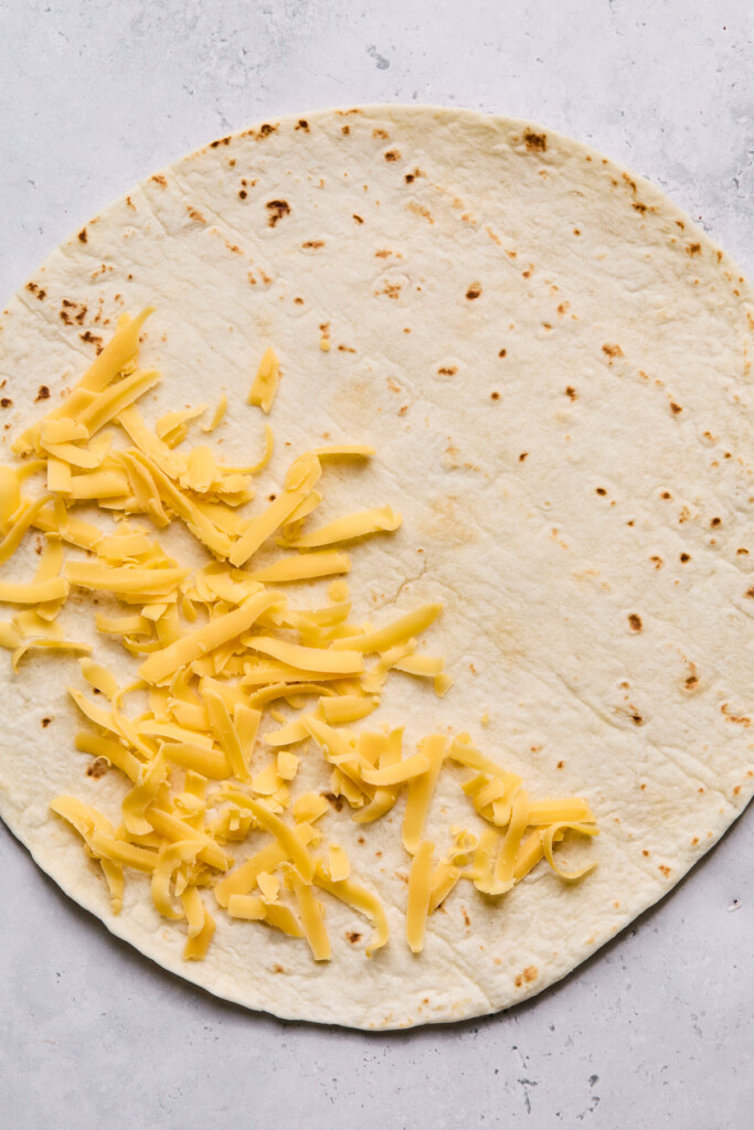 Large tortilla with shredded cheese sprinkled on half of it.
