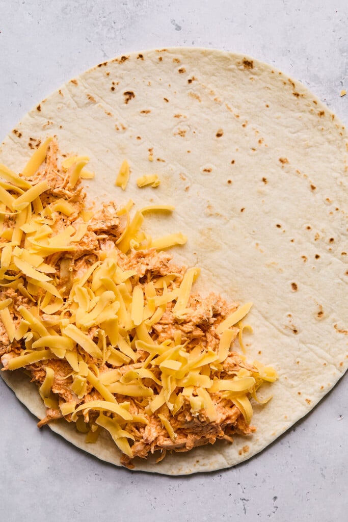 Large tortilla with spicy shredded chicken and shredded cheese sprinkled on half of it.