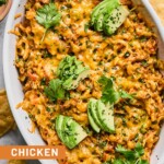 Au gratin dish filled with chicken enchilada dip topped with melted cheese and garnished with cilantro and sliced avocado. Around the dish are some tortilla chips.