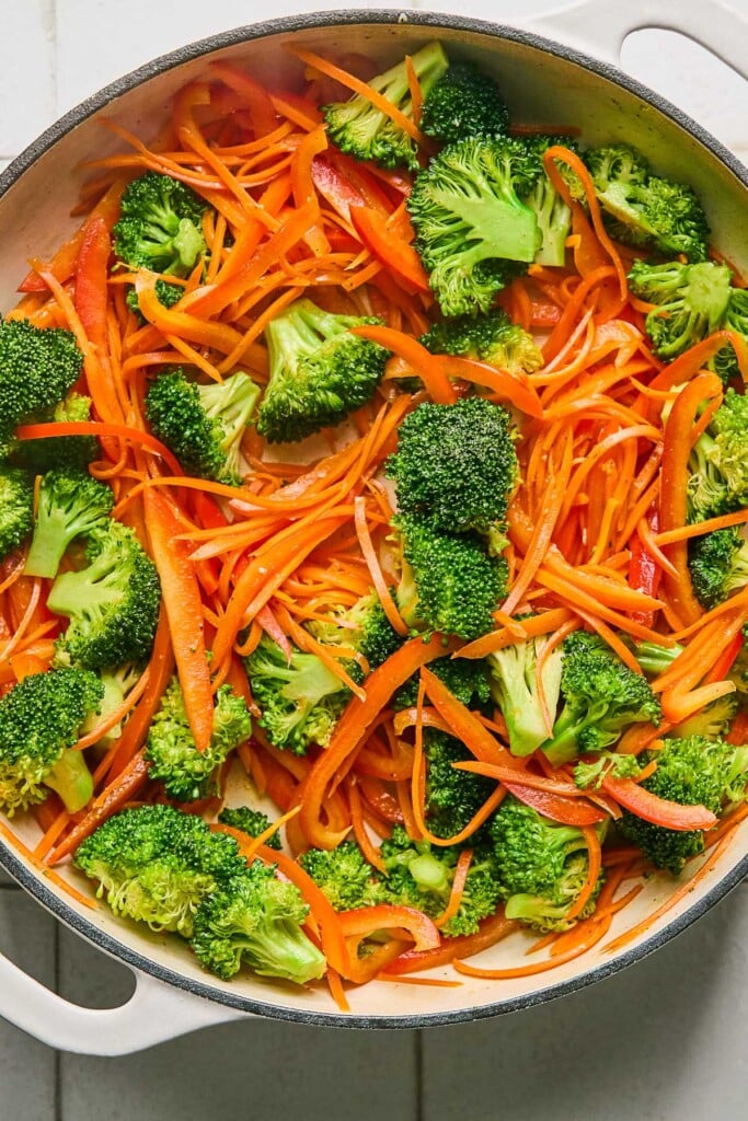 Large white skillet with sautéed broccoli florets, sautéed julienned peppers, and sautéed julienned carrots.