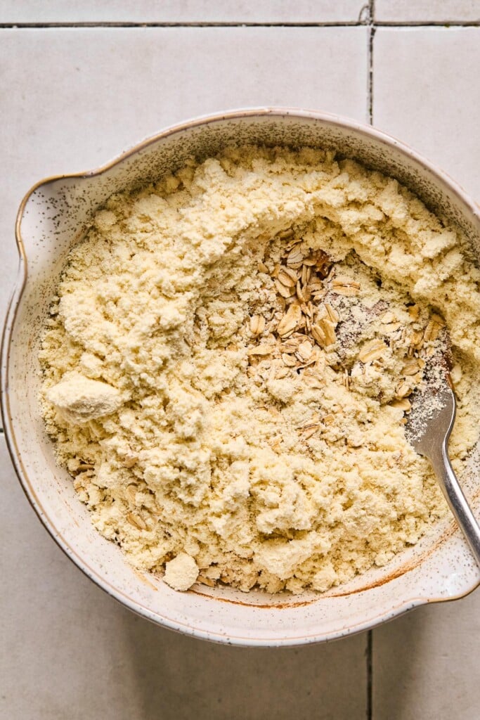 Protein powder overtop a peanut butter mixture in a mixing bowl with a fork in it.
