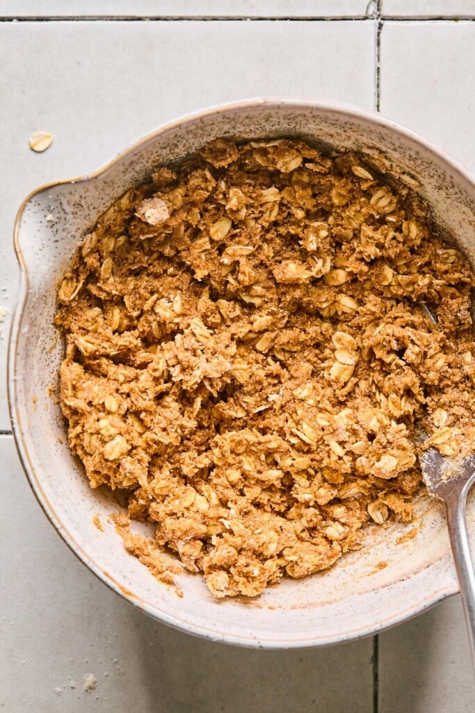 Mixing bowl filled with a batter of oats and peanut butter. A fork is also in the bowl.