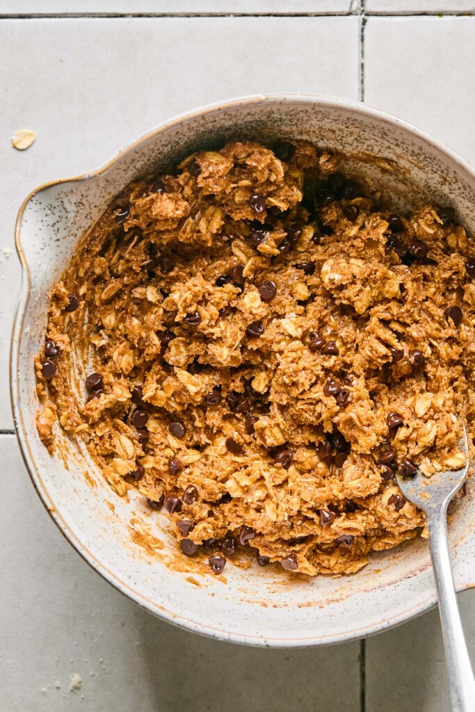 Mixing bowl filled with a batter of oats, peanut butter, and chocolate chips. A fork is also in the bowl.
