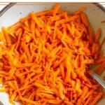Raw carrot salad in a white bowl with a fork in it.
