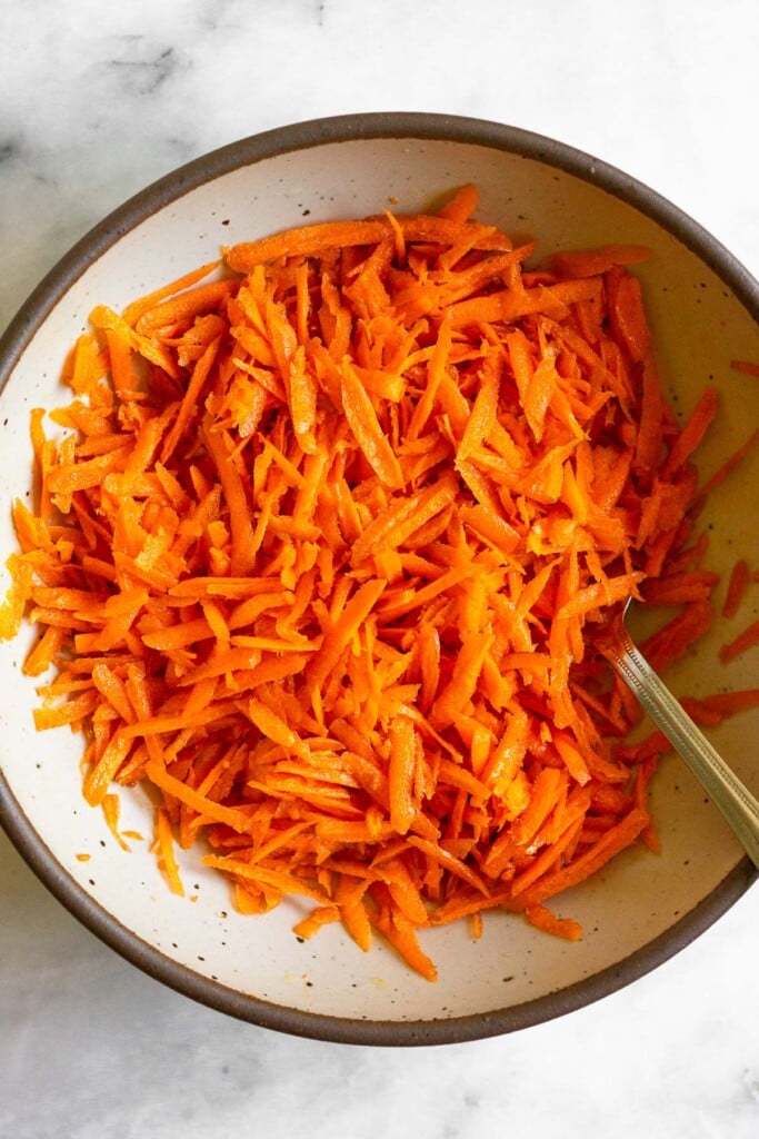 Shredded carrot salad in a white bowl with a fork in it.