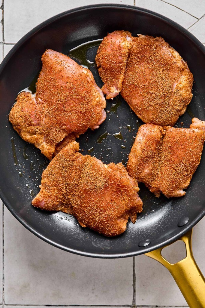 Seasoned chicken things in a large skillet before they are cooked.