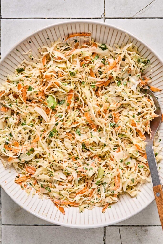 Coleslaw in a large white bowl with a fork in it.