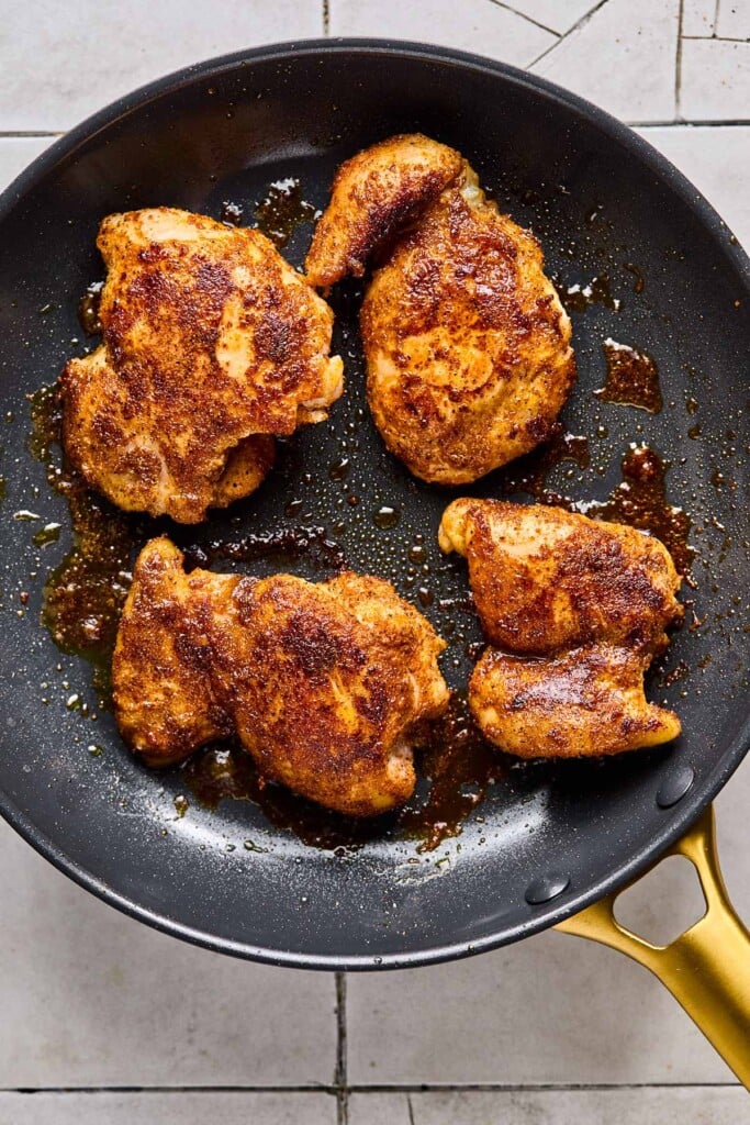 Large skillet with four seasoned and cooked chicken thighs in it.