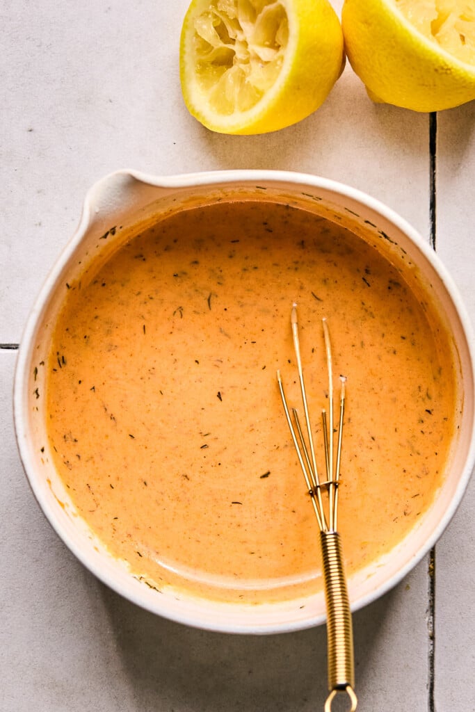 Creamy buffalo sauce in a bowl with a whisk in it. Next to the bowl is a lemon that has been cut in half and juiced.