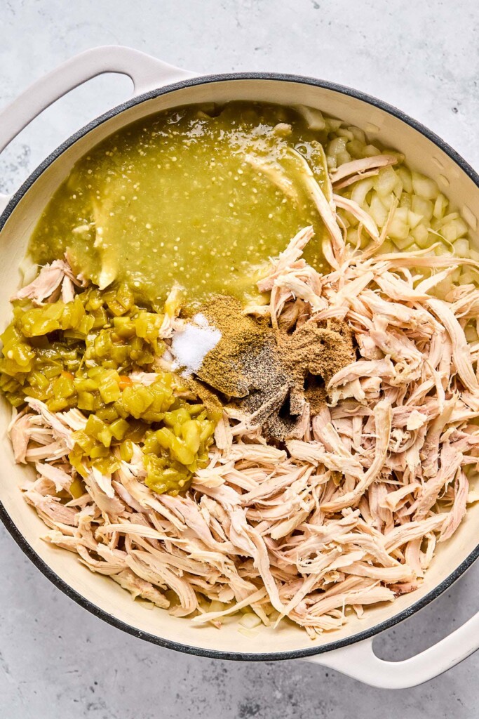 Large enameled pan with sautéed onions, shredded chicken, diced green chiles, green salsa, and spices.