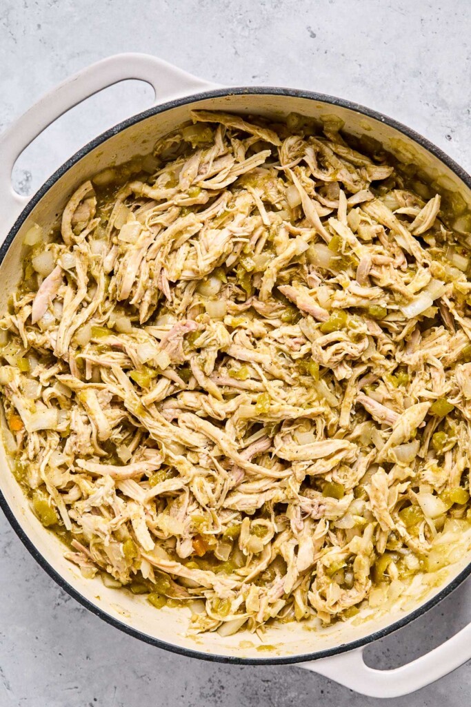 Large enameled pan with a mixture of shredded chicken, sautéed onions, and green salsa.